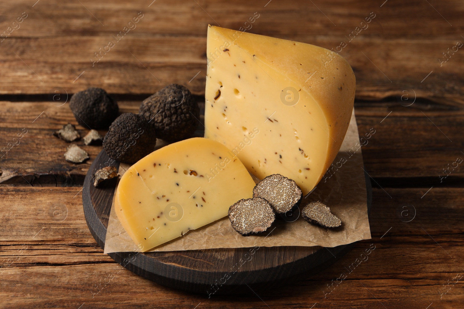 Photo of Board with delicious cheese and fresh black truffles on wooden table