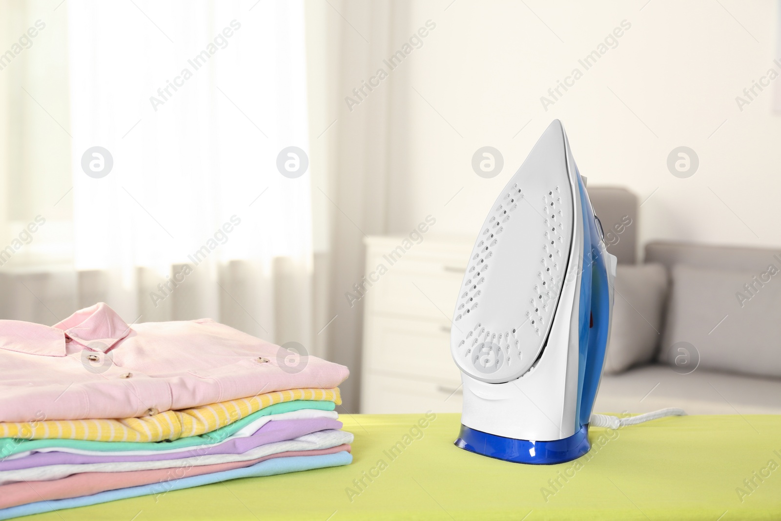 Photo of Board with modern iron and clean laundry at home