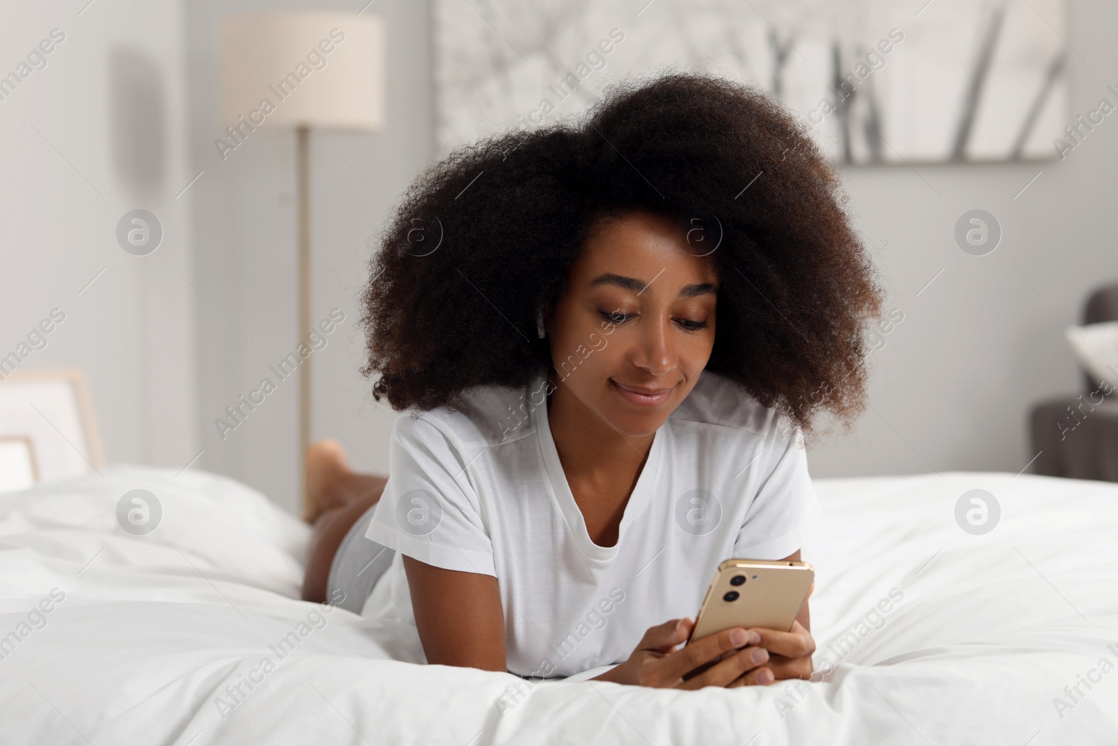 Photo of Beautiful woman in stylish underwear and t-shirt using smartphone on bed indoors