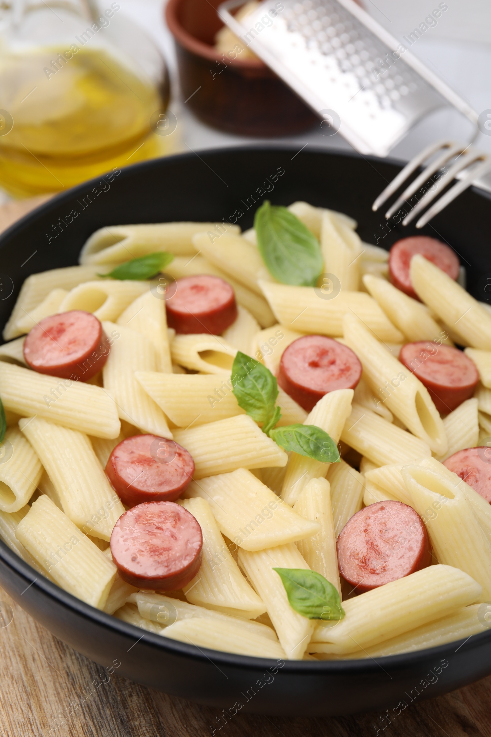 Photo of Tasty pasta with smoked sausage and basil in bowl on table, closeup