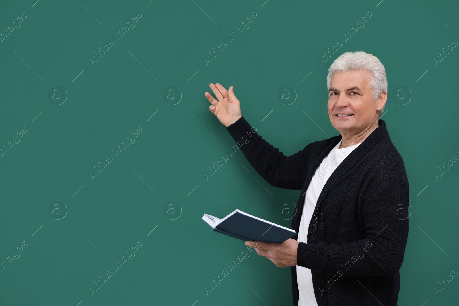 Photo of Portrait of senior teacher with book at green chalkboard, space for text