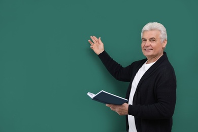 Portrait of senior teacher with book at green chalkboard, space for text