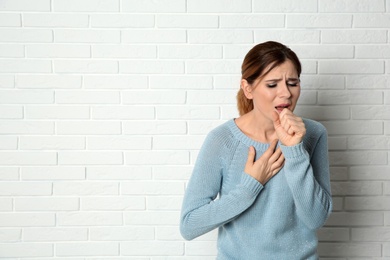 Woman suffering from cough near brick wall. Space for text