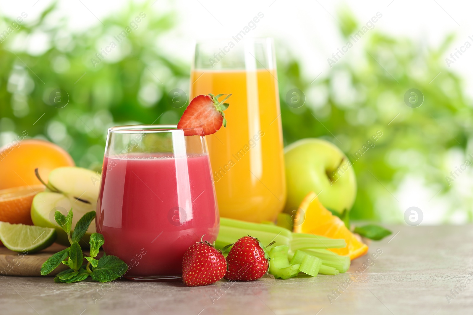 Photo of Glasses with different juices and fresh fruits on table against blurred background. Space for text