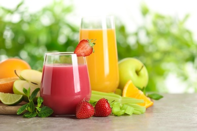 Glasses with different juices and fresh fruits on table against blurred background. Space for text