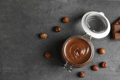 Flat lay composition with tasty chocolate cream in glass jar and hazelnuts on table. Space for text