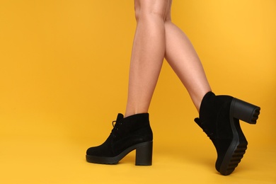 Woman wearing stylish boots on yellow background, closeup