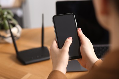 Photo of Woman with smartphone connecting to internet via Wi-Fi router at table indoors, closeup