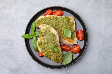 Delicious chicken breasts with pesto sauce, tomatoes and basil on light gray table, top view