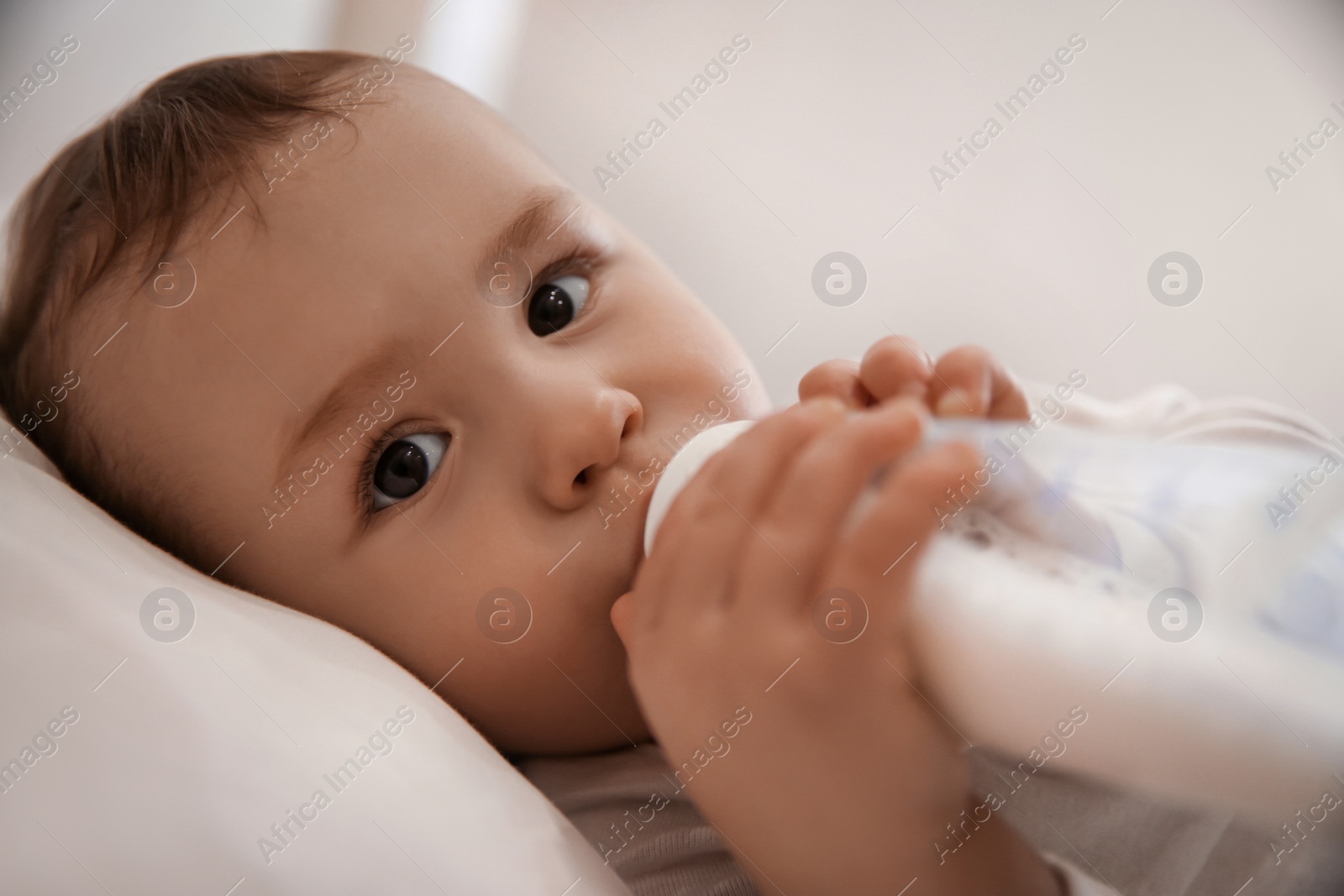 Photo of Cute little baby with bottle lying in comfortable crib. Bedtime