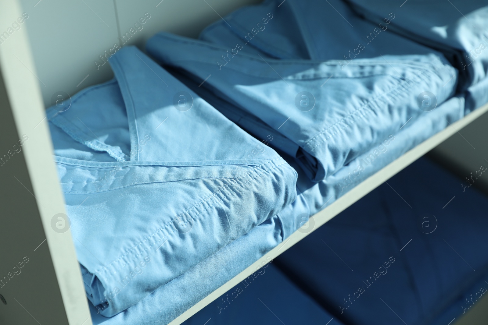 Photo of Light blue medical uniforms on white rack, closeup