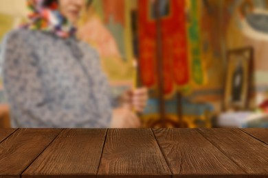 Image of Empty wooden table and blurred view of woman holding candle in church, space for text