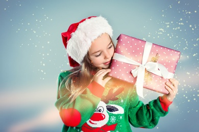 Cute child in Santa hat with Christmas gift on color background