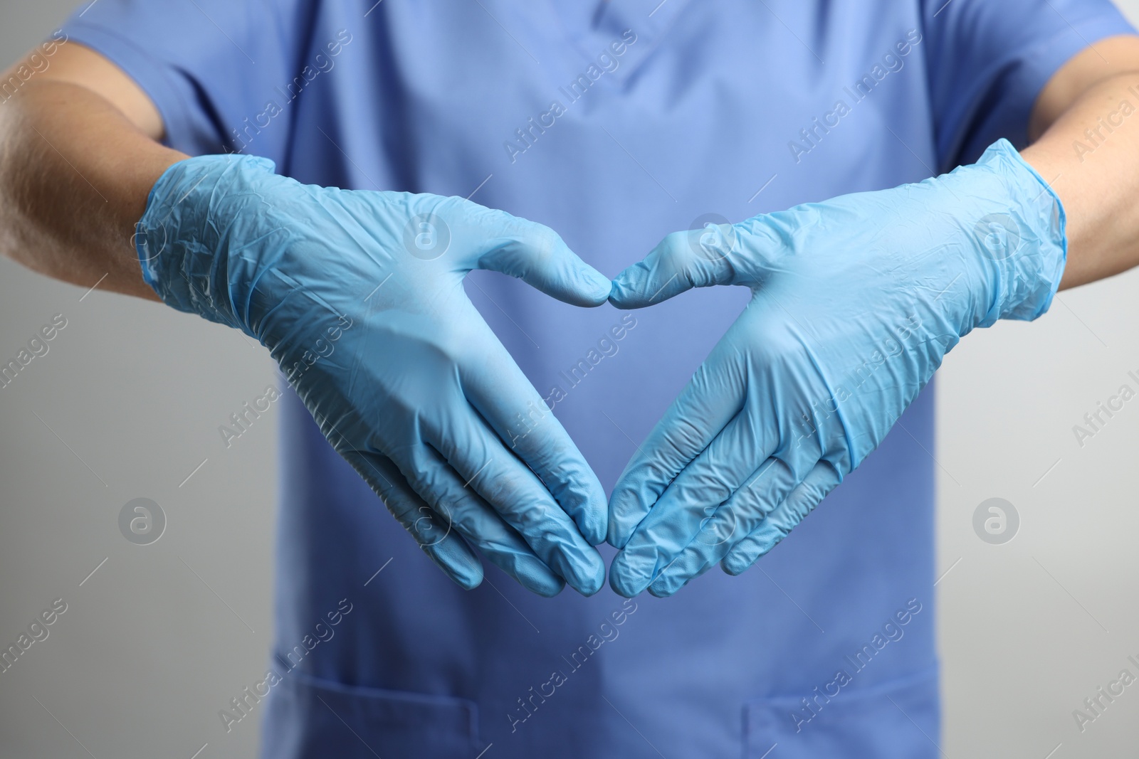 Photo of Doctor wearing light blue medical gloves making heart gesture on grey background, closeup