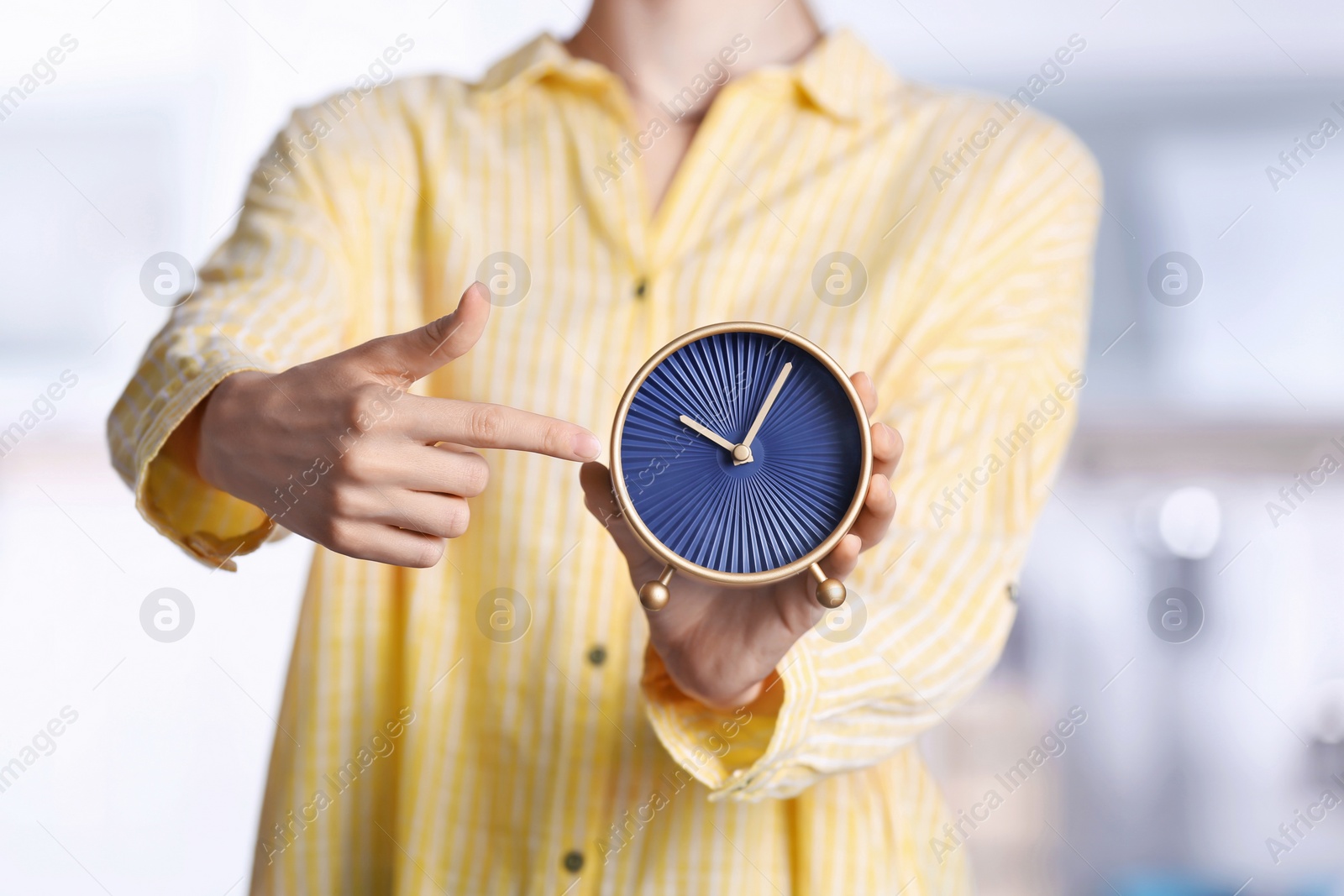 Photo of Young woman holding alarm clock on blurred background. Time concept