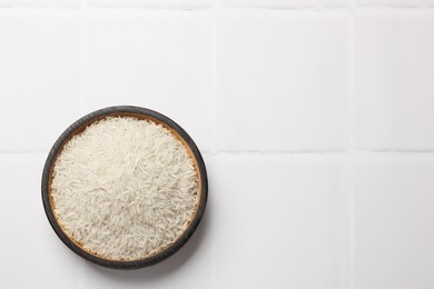 Photo of Raw basmati rice in bowl on white tiled table, top view. Space for text