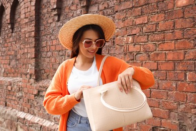 Young woman with stylish bag near red brick wall outdoors