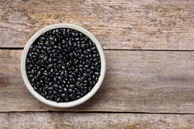 Bowl of raw black beans on wooden table, top view. Space for text