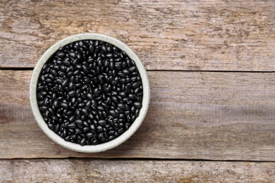 Photo of Bowl of raw black beans on wooden table, top view. Space for text