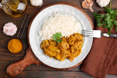 Photo of Delicious chicken curry with rice and ingredients on wooden table, flat lay