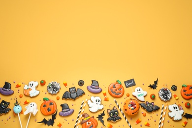 Flat lay composition with decorated gingerbread cookies on yellow background, space for text. Halloween celebration