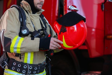Firefighter in uniform with helmet near red fire truck at station, closeup