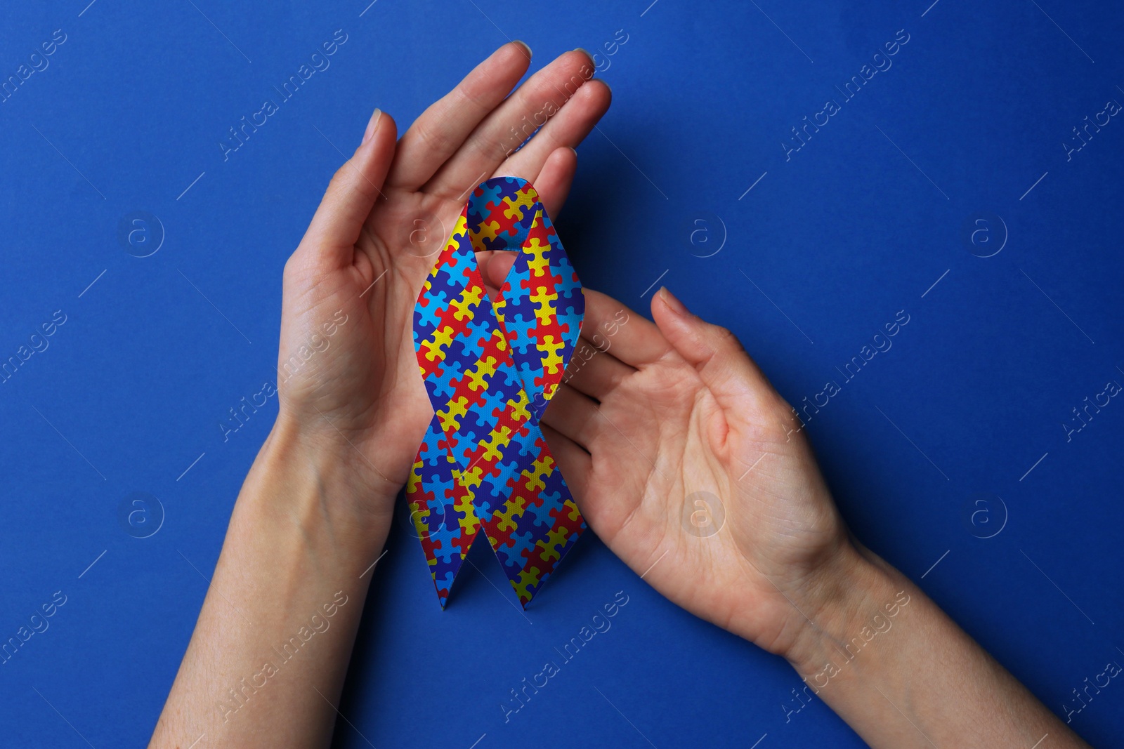 Image of World Autism Awareness Day. Woman with colorful puzzle ribbon on blue background, top view
