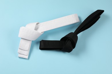 White and black karate belts on light blue background, flat lay