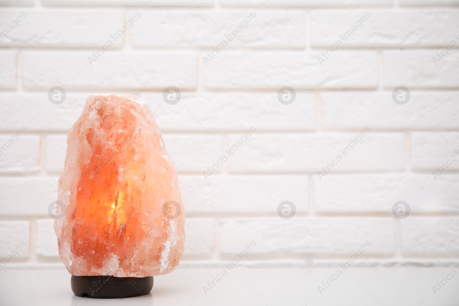 Photo of Himalayan salt lamp on table near white brick wall. Space for text