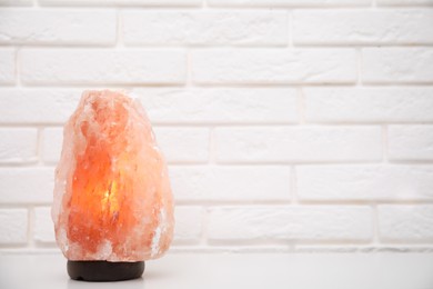 Photo of Himalayan salt lamp on table near white brick wall. Space for text