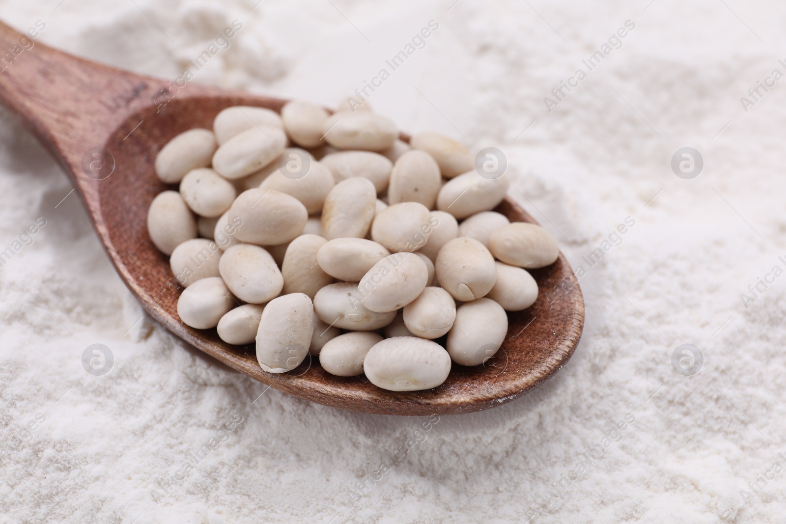 Photo of Wooden spoon with white kidney beans on flour, closeup