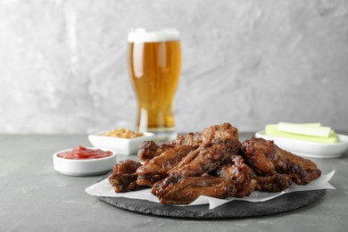 Delicious chicken wings served with glass of beer on grey table