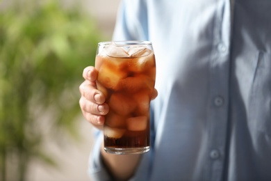 Photo of Woman holding glass of cola with ice on blurred background, closeup. Space for text