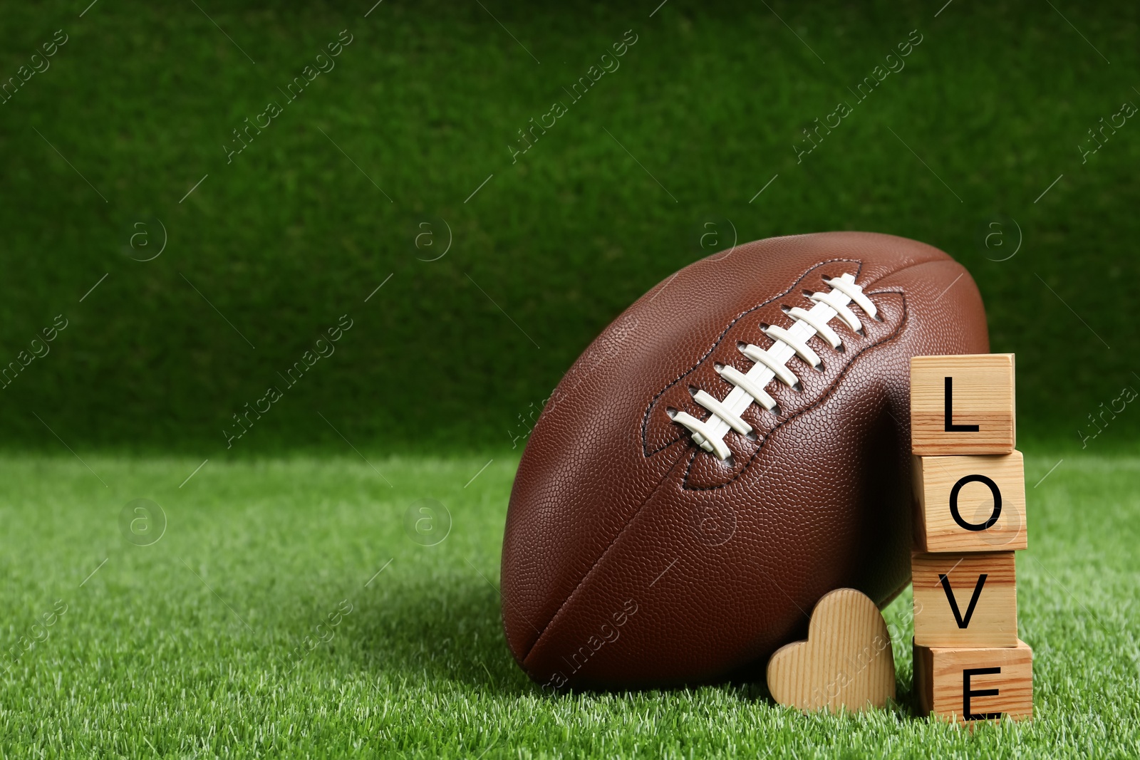 Photo of American football ball, cubes with word Love and heart on green grass. Space for text