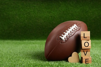 Photo of American football ball, cubes with word Love and heart on green grass. Space for text