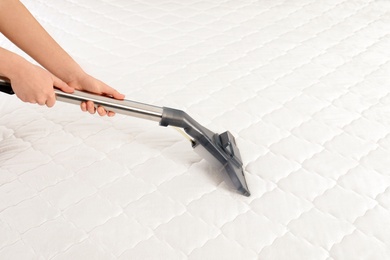 Photo of Woman disinfecting mattress with vacuum cleaner, closeup. Space for text
