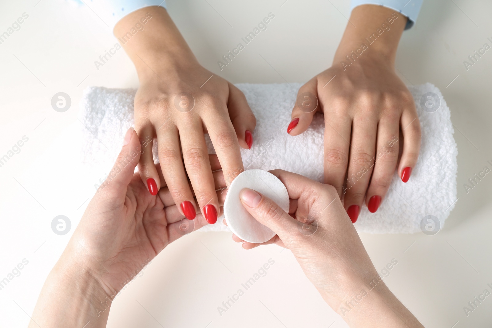 Photo of Manicurist removing polish from client's nails on white background, top view