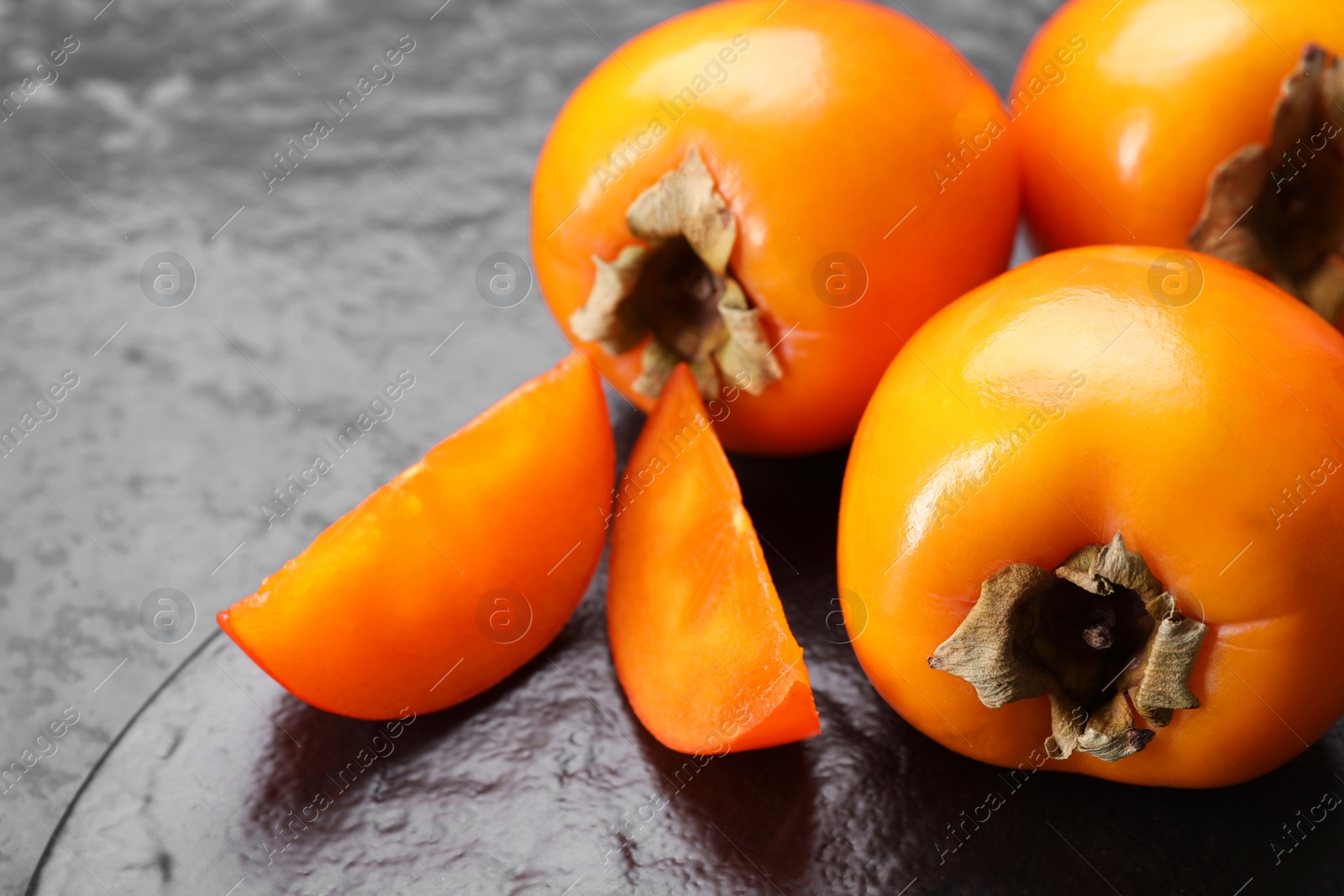 Photo of Delicious ripe persimmons on dark textured table, closeup