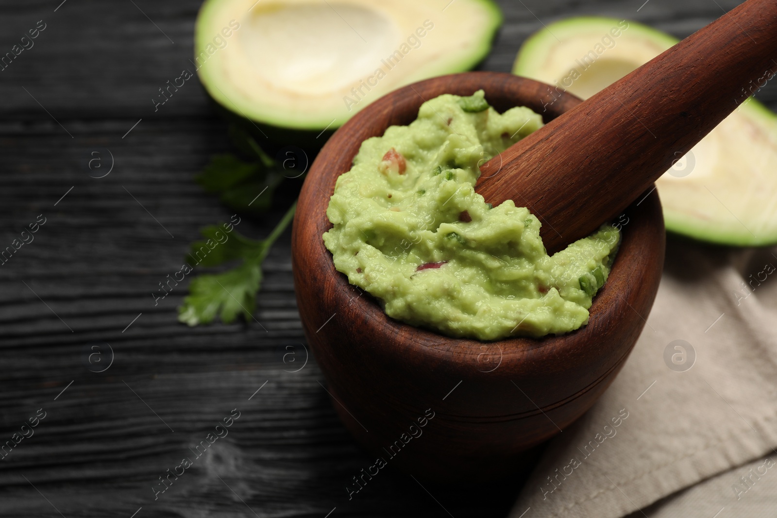 Photo of Mortar with delicious guacamole and ingredients on black wooden table, closeup. Space for text