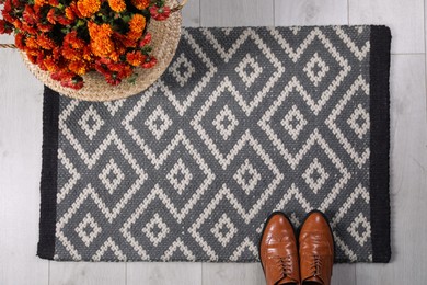 Stylish door mat with shoes and beautiful flowers on floor, flat lay