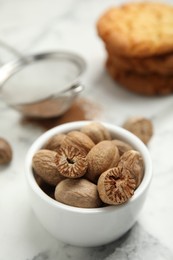 Photo of Nutmeg seeds in bowl on white marble table, closeup