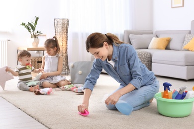 Photo of Housewife cleaning carpet while her children playing in room