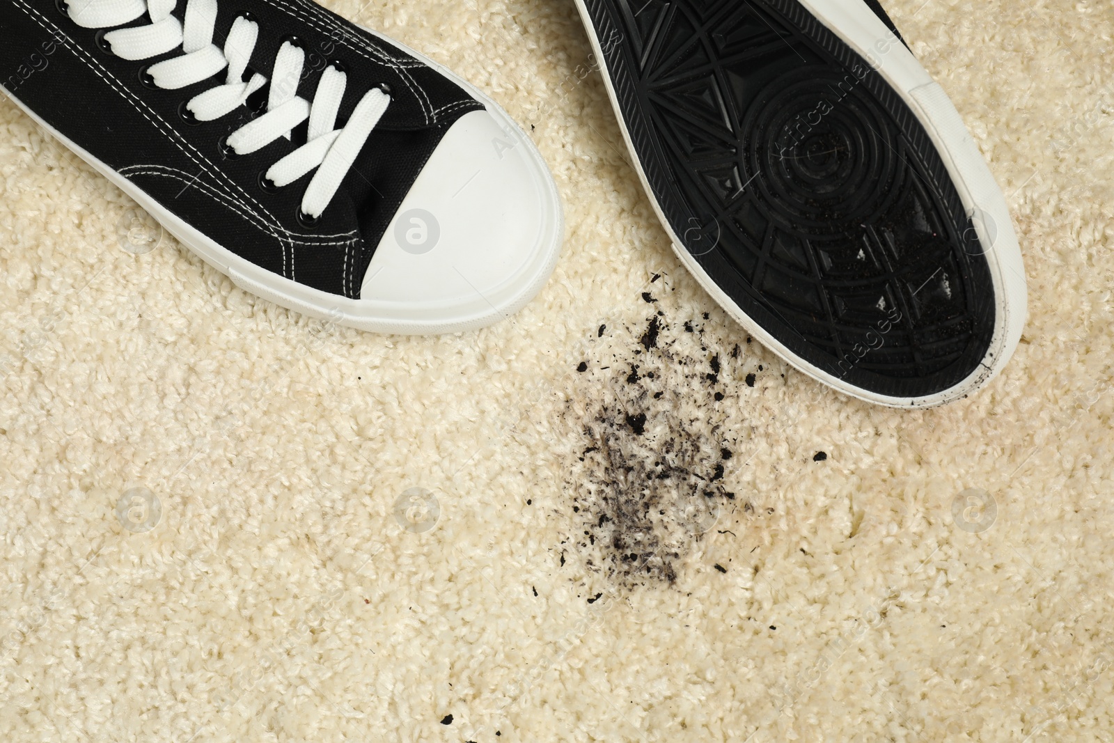 Photo of Black sneakers and mud on beige carpet, top view