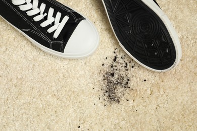 Black sneakers and mud on beige carpet, top view