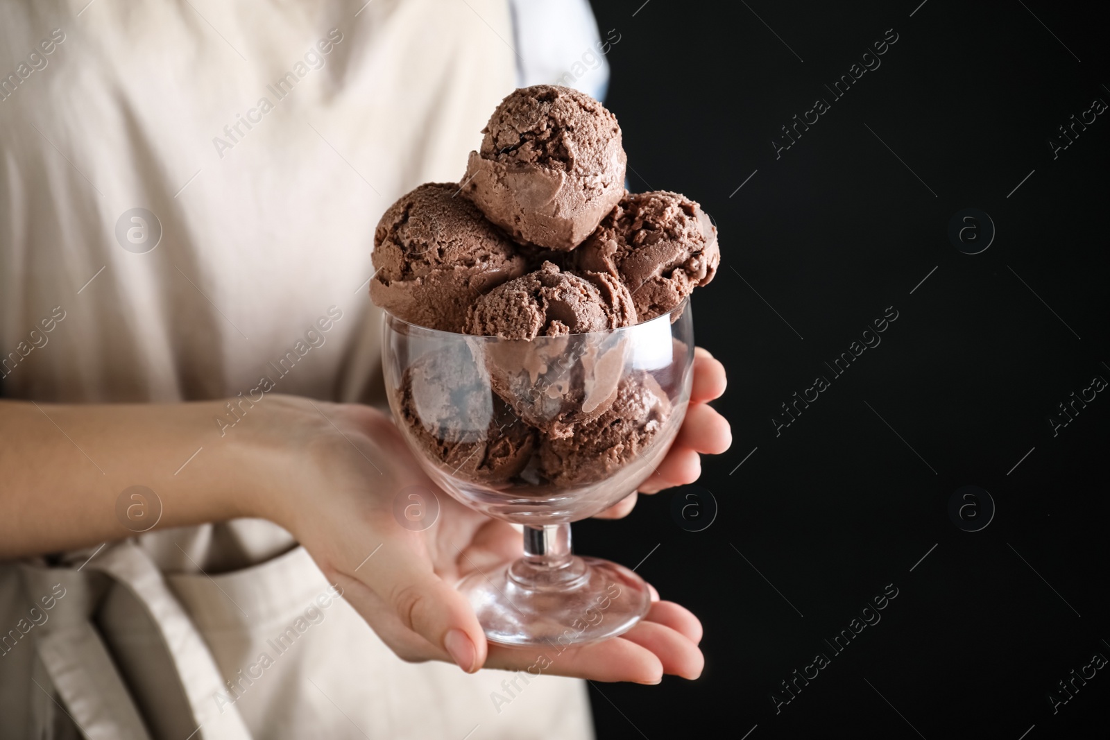 Photo of Woman holding glass bowl full of chocolate ice cream on black background, closeup. Space for text