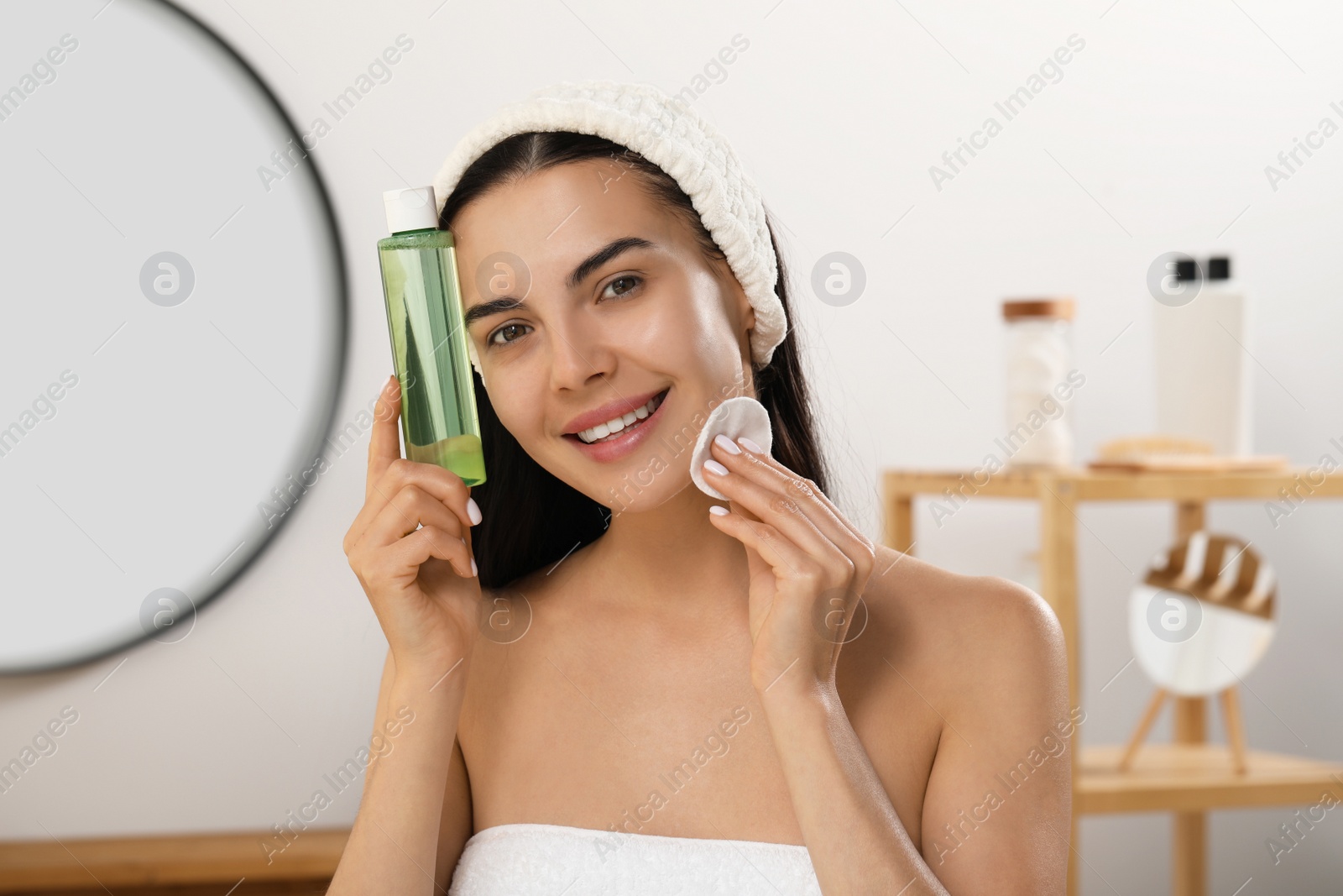 Photo of Young woman using cotton pad with micellar water indoors