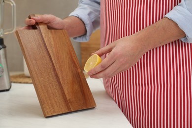 Man with wooden cutting board and lemon at light table in kitchen, closeup