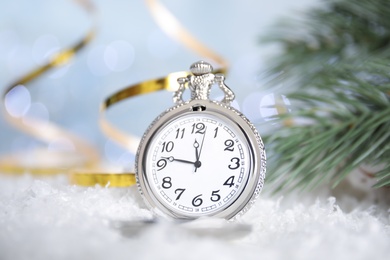 Photo of Pocket watch, golden serpentine streamers and fir branch on snow against blurred lights. New Year countdown