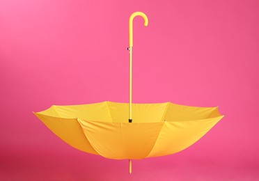 Stylish open yellow umbrella on pink background
