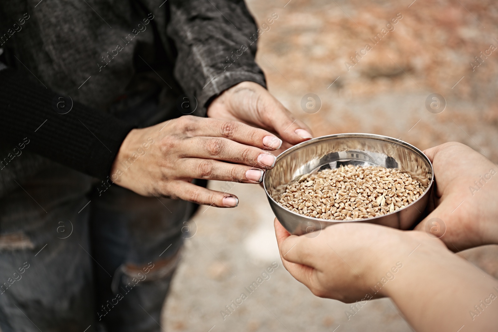 Photo of Woman giving poor homeless person bowl of wheat outdoors, closeup